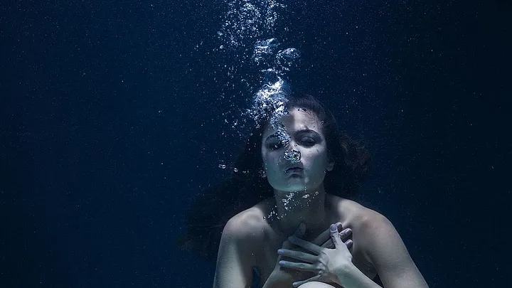 nude person blowing bubbles underwater, hands clutched to throat