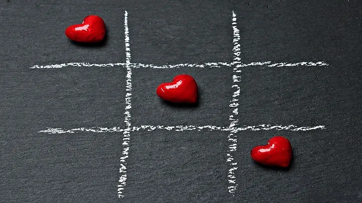 three red heart-shaped candies on a chalk-drawn tic-tac-toe grid