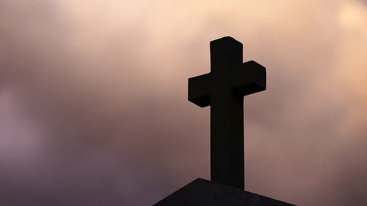 large cross on a pointed roof seen against a pink cloudy sky