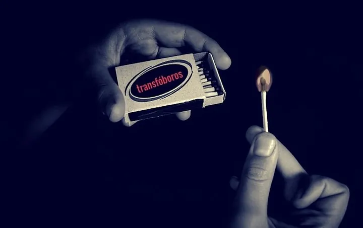 One hand holds an open matchbox, the other holds a struck match. The matchbox brand label is "transfóboros."