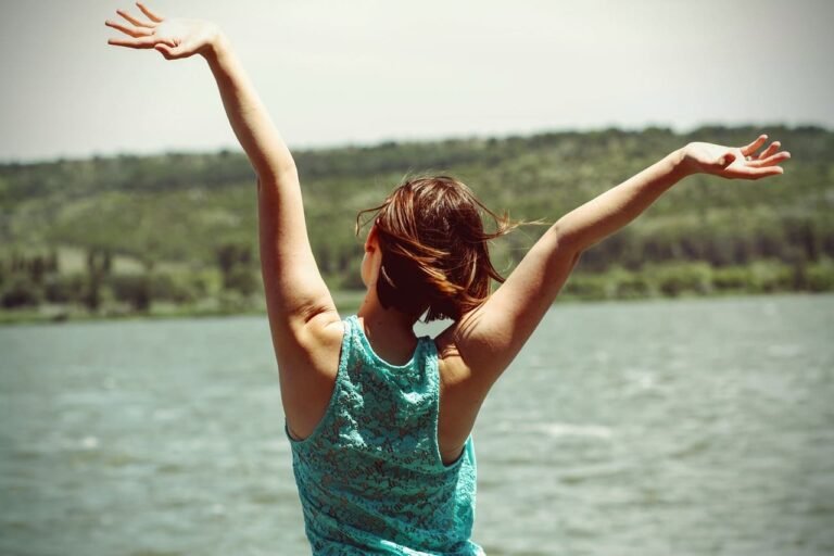 person raising arms to sky by a lake, suggesting freedom