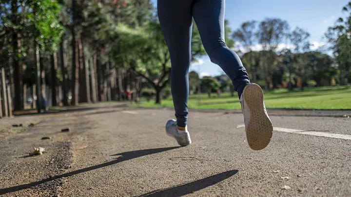 A runner's legs. The person is jogging alone down a tree-lined street.