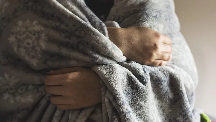 A person wraps themself in a gray blanket. You can only see their hands.