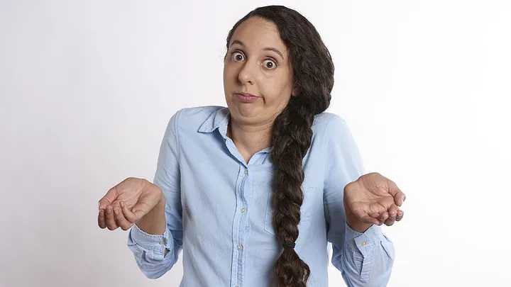 person with a long braid lifts both palms in the air and looks comically confused