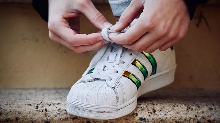 hands tying white sneaker with colorful stripes