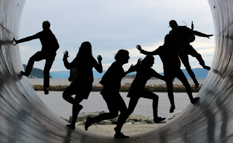 six people running and jumping for fun in a large tunnel, with the great outdoors visible behind them