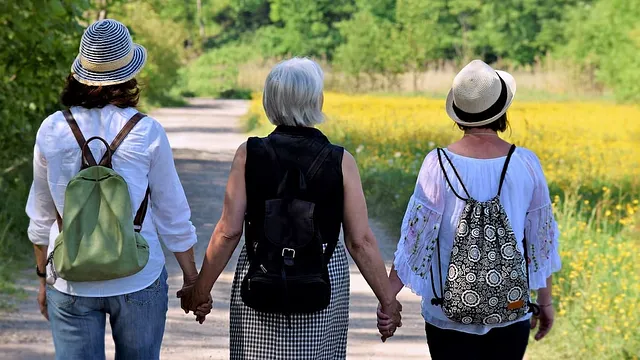 three women walk hand-in-hand down a path by a meadow