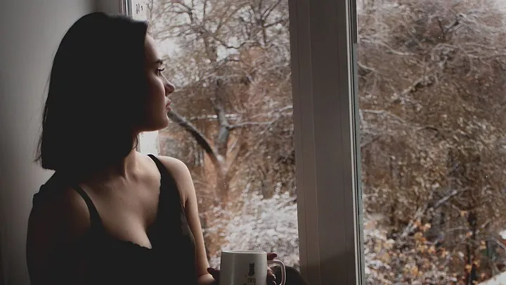 person holding coffee cup sitting by window