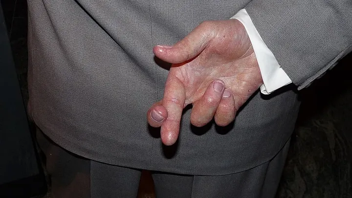 person in a formal gray suit, crossing their fingers behind their back