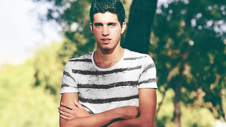 adult standing outdoors in T-shirt with arms folded