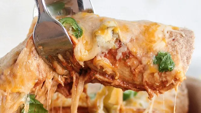 silver fork and spoon pry an enchilada, smeared with red sauce, yellow cheese and green chilis, and lift the gooey creation off the plate