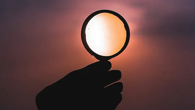 person holds up a magnifying glass to the sunset. the sunlight seen through the magnifying glass is a different color.