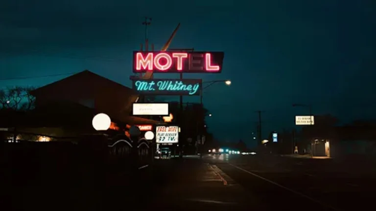 Motel with a neon sign on a road with little traffic at night. MOT-L is lit up. The E is dark.