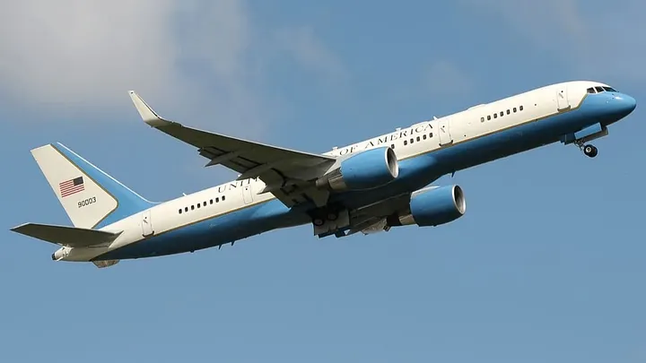 plane in flight. United States of America is painted on it. there's a US flag on the tail.